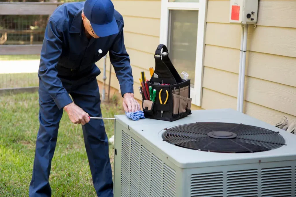 HVAC technician performing maintenance on outdoor air conditioning unit using tools for inspection and repair.