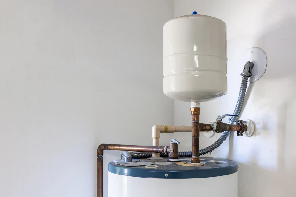 Residential hot water tank with expansion tank and copper plumbing connections installed in a utility room, showing a typical water heater setup near the end of its service life.