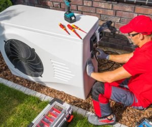 Professional Middle Aged HVAC Technician in Red Uniform Repairing Modern Heat Pump Unit. House Heating and Cooling System Theme.