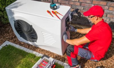 Professional Middle Aged HVAC Technician in Red Uniform Repairing Modern Heat Pump Unit. House Heating and Cooling System Theme.
