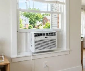 How to install a window AC unit in a double-hung window with accordion side panels, power cord plugged into wall outlet, bright suburban home interior