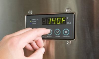 "A male finger is turning up the temperature on a tankless water heater control panel. Tankless water heaters are new technology which produces hot water on demand and is much more energy efficient than a conventional hot water holding tank system. This unit is installed and in operation, there are some scratches, dust and scuff marks on the surface."